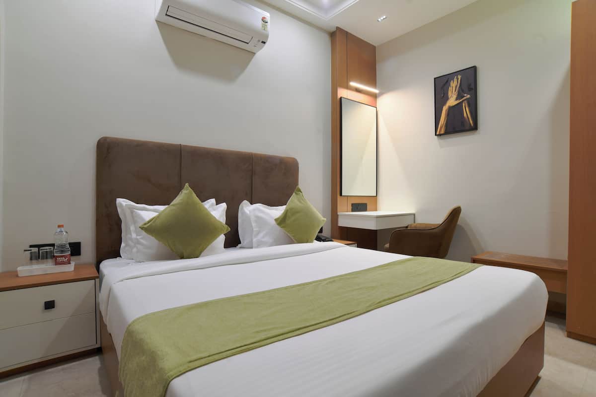 Ein Hotelzimmer mit einem großen Bett, einem Nachttisch, einem Schreibtisch, einem Sessel und einer Wand-Klimaanlage.