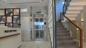 Zona de recepción con mostrador identificado como "RECEPTION", una escalera con barandillas de madera y un ascensor con un panel de espejo.