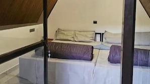 A bedroom with a sloped ceiling, a bed with white bedding and purple pillows, and a small bedside table. - The Soul of vattavada (Devikolam)