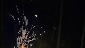 A campfire with logs and sparks, surrounded by a dirt ground. - The Soul of vattavada (Devikolam)
