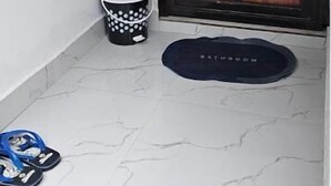 A bathroom with a white sink, a mirror, a black bucket, and a blue mat. - The Soul of vattavada (Devikolam)