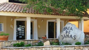 A stone wall with a sign reading "BAJA DE BAHAS" in front of a building with a tiled roof and columns. - THREE-ROOM APARTMENT HOUSE EMY C11 GROUND FLOOR WITH PATIO AND GARDEN (Golfo di Marinella)