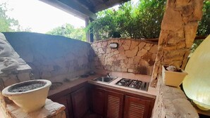 A small outdoor kitchen with a stone wall, a sink, and a gas stove. - THREE-ROOM APARTMENT HOUSE EMY C11 GROUND FLOOR WITH PATIO AND GARDEN (Golfo di Marinella)