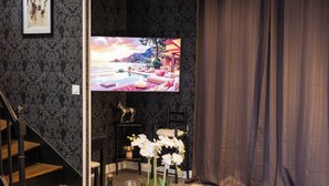 Un salon moderne doté d’un grand téléviseur à écran plat, d’un escalier en bois, d’un ensemble de canapés et d’une plante orchidée en pot.