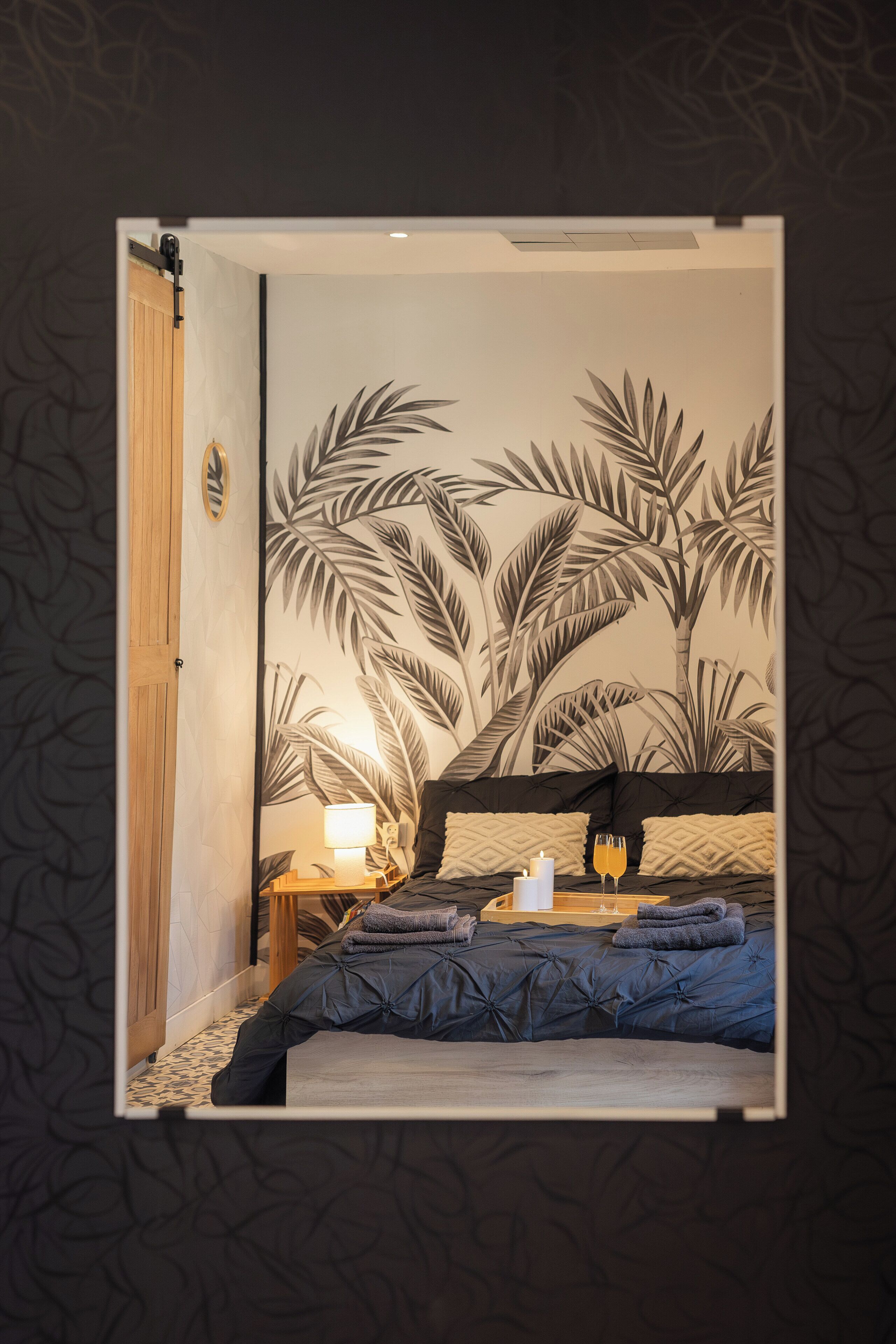 A room with a bed, a nightstand with a lamp, and a wall with a tropical leaf pattern.