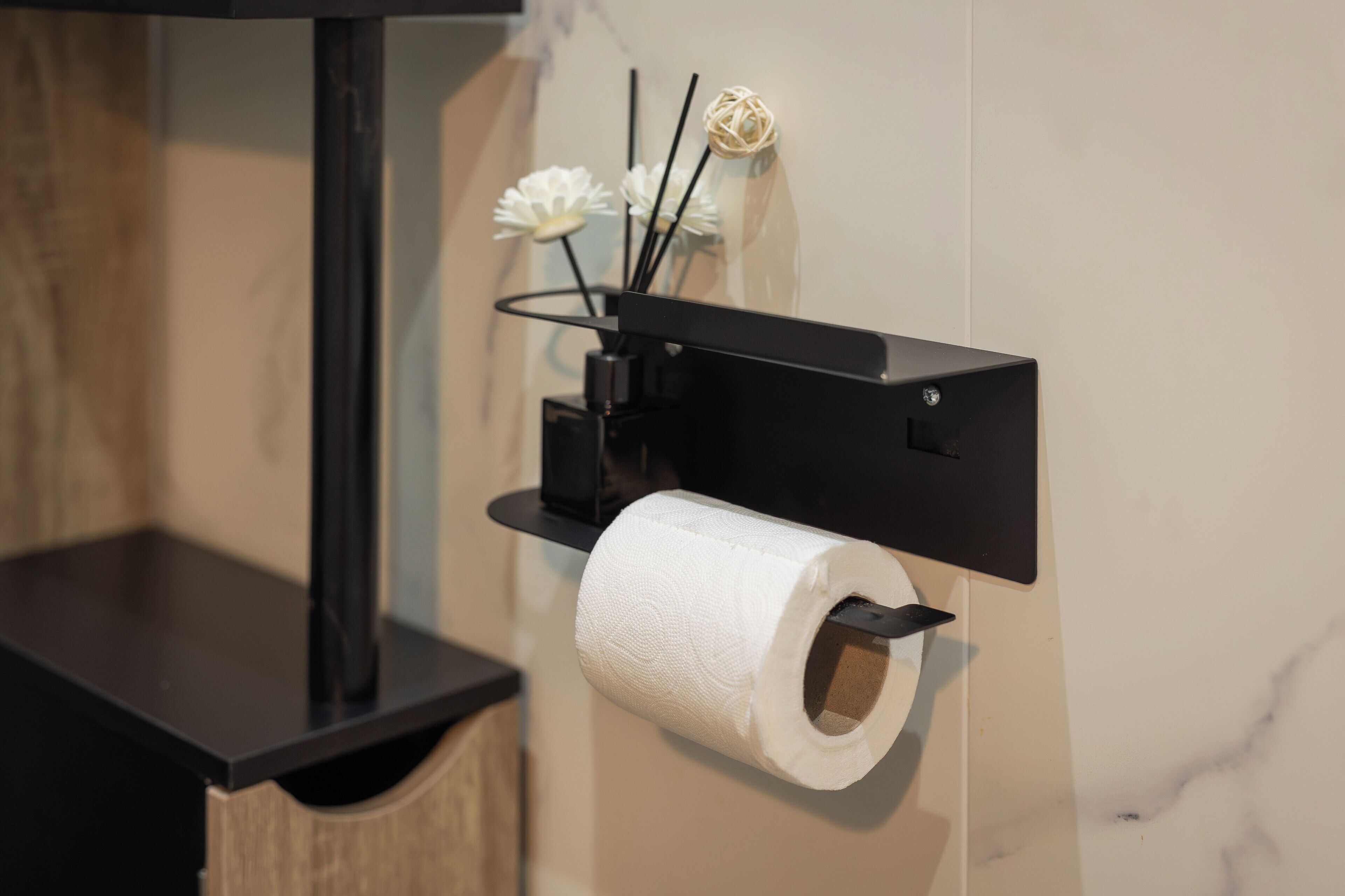 A toilet paper holder with a roll of toilet paper and decorative items on a black wall.