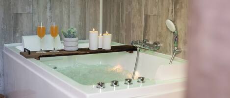 A bathtub with candles, a plant, and two glasses of orange juice.