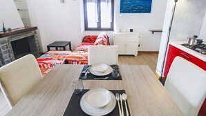 Ein kompaktes Hotelzimmer mit Bett, Esstisch für zwei Personen, einer Küchenzeile und einem Bild an der Wand.