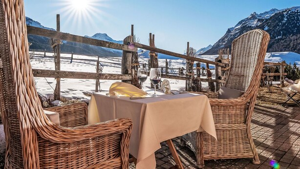 An outdoor seating area with wicker chairs and a table, overlooking a snowy landscape and mountains. - Beautiful apartment for 5 guests with TV, patio, pets allowed and panoramic view (Silvaplana)