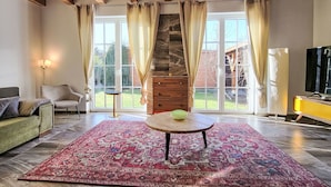 Un salon spacieux avec une grande fenêtre, un plafond en bois, une table ronde et un téléviseur.