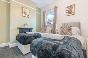 A hotel room with two beds, a window with curtains, a bedside table with a clock, and artwork on the walls. - Spacious Warwick Stay | Contractors & Families (Warwick)