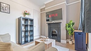 A living room with a fireplace, a bookshelf, and a television displaying 'NETFLIX'. - Spacious Warwick Stay | Contractors & Families (Warwick)
