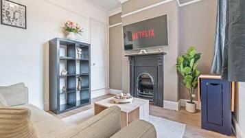 A living room with a fireplace, a bookshelf, and a television displaying 'NETFLIX'.