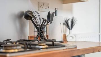 A kitchen counter with a gas stove, a utensil holder, and a white vase with decorative branches.