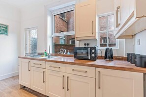A kitchen with white cabinets, a microwave, a kettle, and a window with a view of a brick building. - Spacious Warwick Stay | Contractors & Families (Warwick)