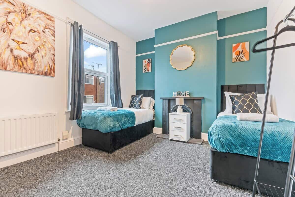 A bedroom with two beds, a window with curtains, a radiator, and artwork on the walls.