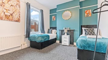 A bedroom with two beds, a window with curtains, a radiator, and artwork on the walls.