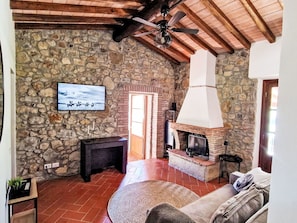 Ein rustikales Interieur mit einer Steinwand, einem Kamin, einem an der Wand befestigten Fernseher und einem Deckenventilator.