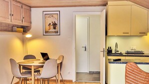Une cuisine de taille réduite avec des meubles en bois, un coin repas comprenant une table et des chaises, et une porte donnant sur une autre pièce.