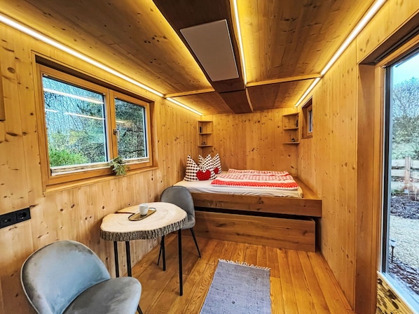 Ein gemütliches Cabin-Zimmer mit einem Bett, einem kleinen Tisch, zwei Stühlen und einem Fenster.
