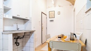A compact kitchen with white cabinets, a sink, and a dining area with a table and chairs. - Termini Volte Antiche & Comfort (Rome)