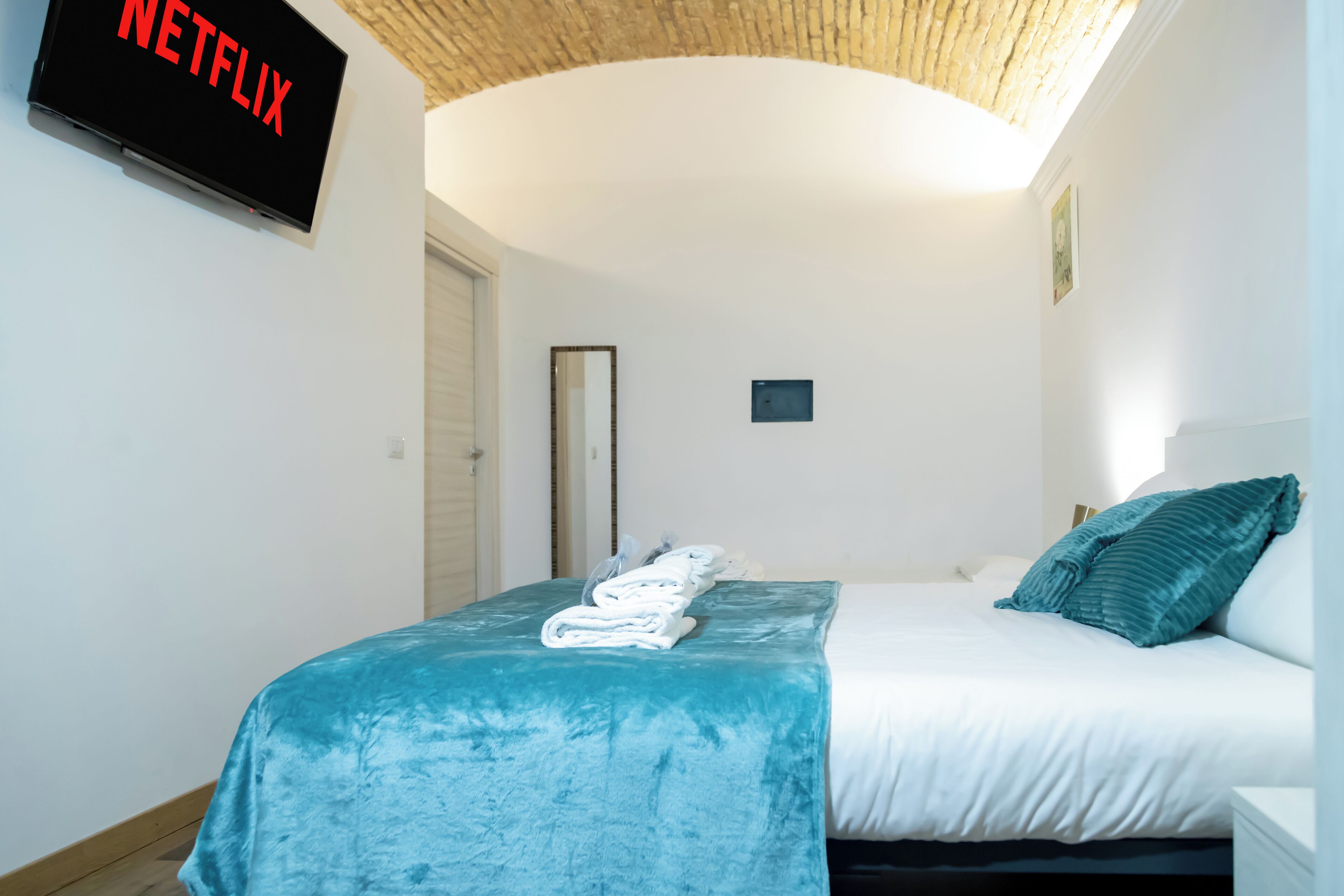 A hotel room with a bed, a TV mounted on the wall, and a ceiling with a woven texture.