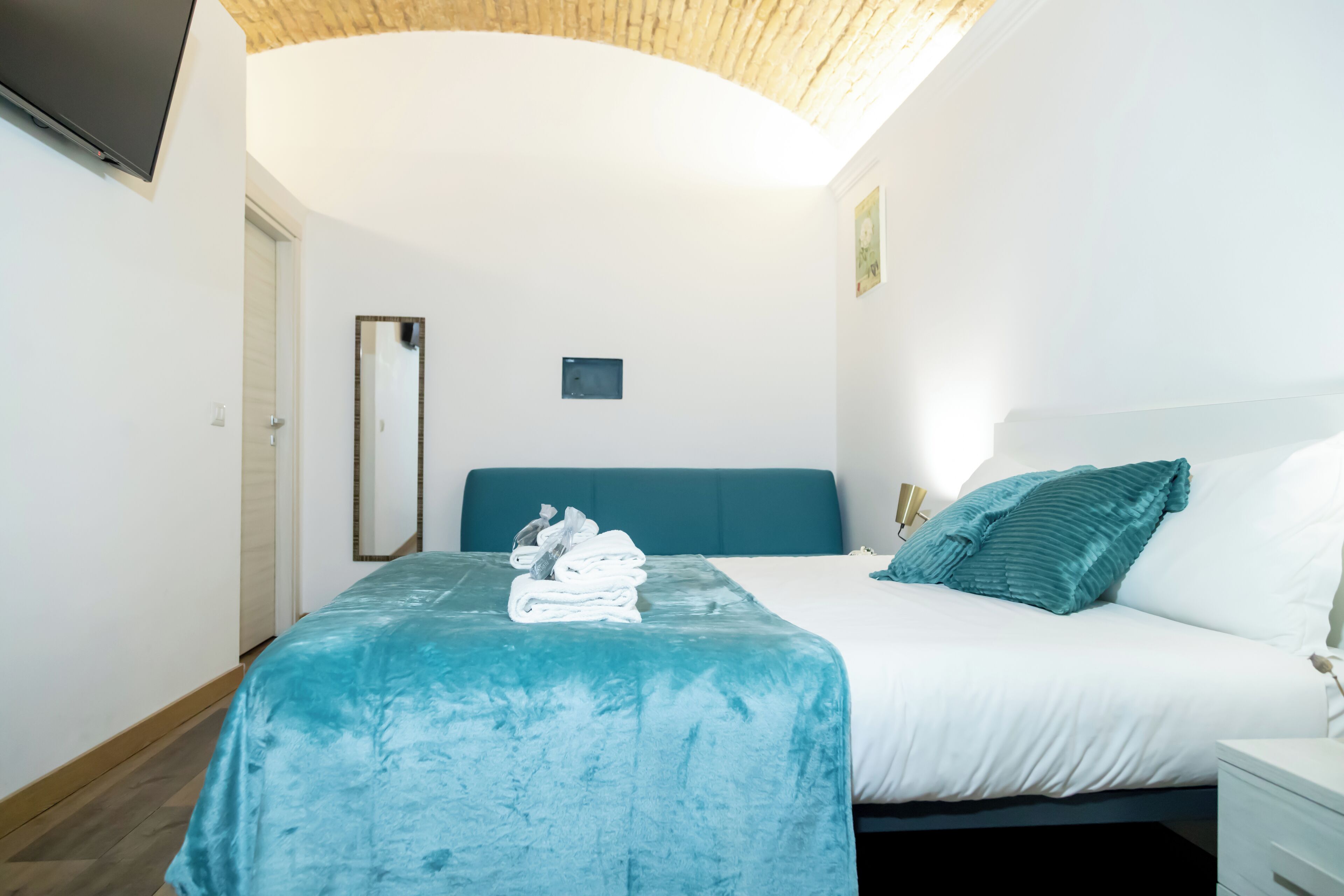 Une chambre d’hôtel moderne dotée d’un grand lit, d’un téléviseur à écran plat fixé au mur et d’un plafond au décor en bois.