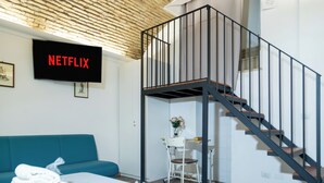 A modern hotel room with a blue sofa, a bed with neatly folded white towels, a desk with a chair, and a staircase with a black railing. - Termini Volte Antiche & Comfort (Rome)