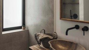 Une salle de bain moderne dotée d’une grande fenêtre, d’un meuble-lavabo en bois avec un vasque en pierre et d’un miroir avec un robinet noir.