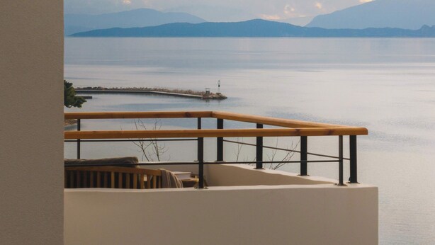 Un balcon doté d’une balustrade en bois, donnant sur une étendue d’eau calme et sur des montagnes lointaines.