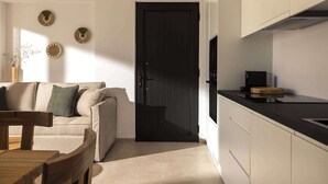 Une cuisine moderne avec des armoires blanches, un comptoir noir et une cuisinière intégrée. Le salon adjacent est doté d’un canapé beige, d’une table en bois et de chaises.