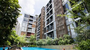 A modern apartment building with a swimming pool and lush greenery.