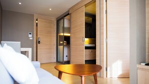 A modern hotel room with a sofa, a wooden coffee table, a wardrobe, and a small table with a laptop.