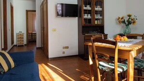 Un comedor con una mesa de madera, sillas, un televisor montado en la pared y un armario con puertas de cristal.