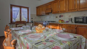 Una cocina con armarios de madera, un microondas y una mesa lista para comer, con platos, vasos y una botella.