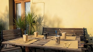 Ein Holztisch ist gedeckt mit zwei beigen Tassen, einem Metallbecher und Besteck auf gewebten Tischsets.