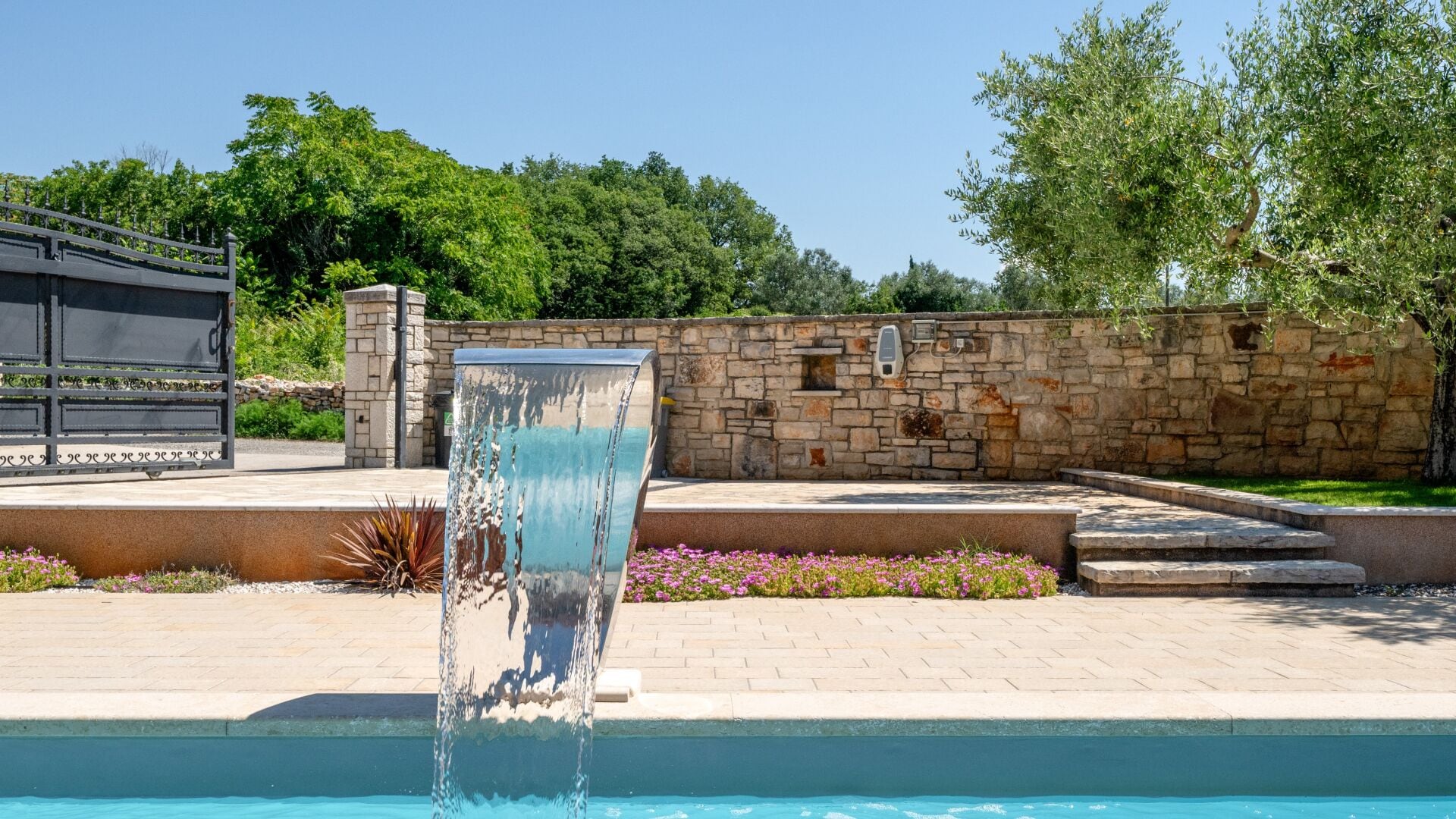 A pool with a water feature, stone walls, and a pergola.