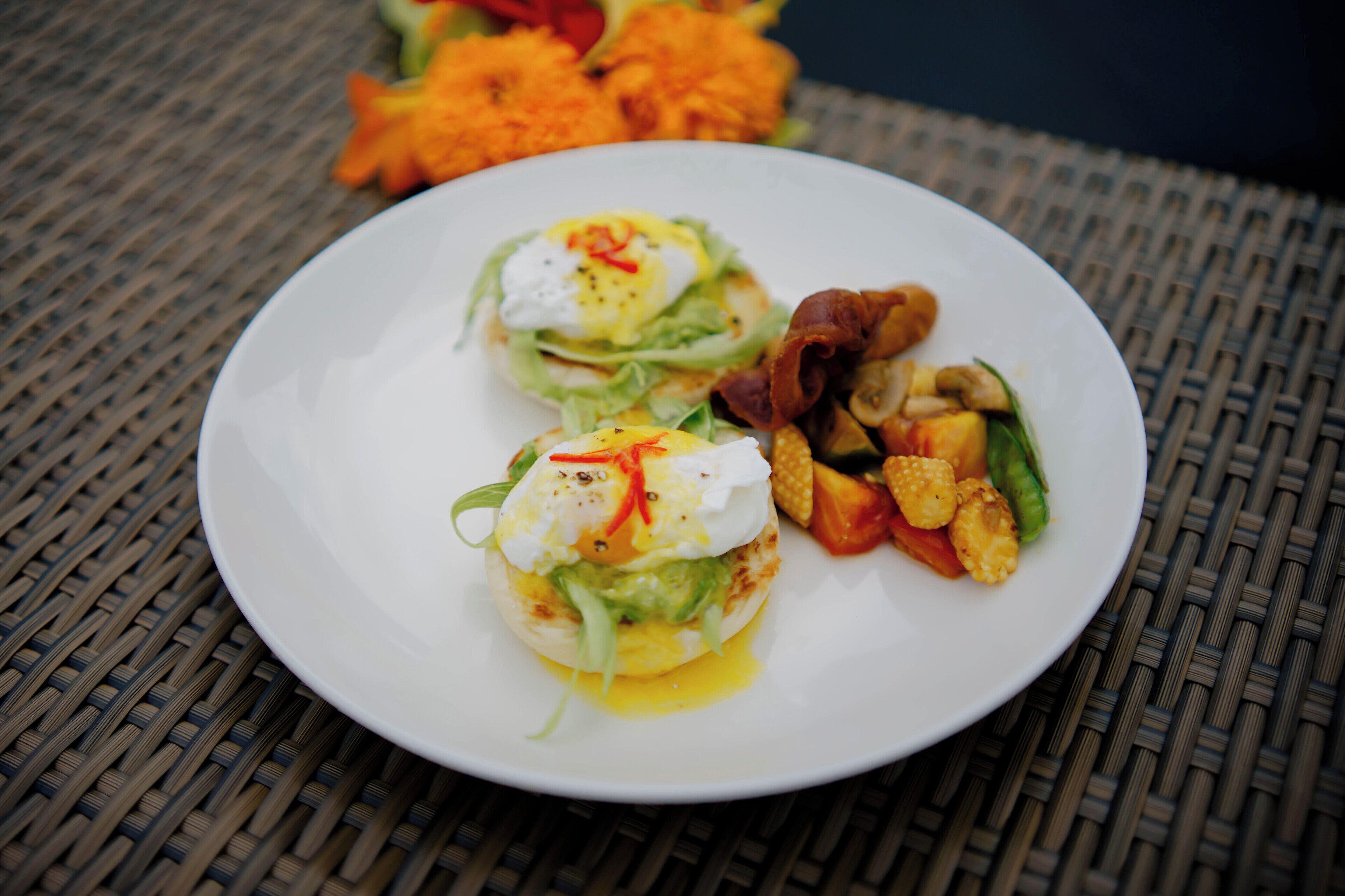 A plate with two poached eggs, avocado, and greens on a woven table mat.