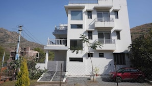 A multi-story residential building with balconies, a gated entrance, and a red car parked in front. - The Nivaas At Jagir Villa (Udaipur)