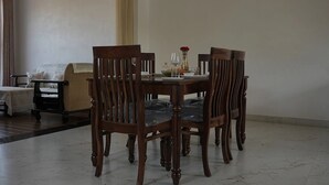 A dining area with a round wooden table and four chairs, a sofa, and a clock on the wall. - The Nivaas At Jagir Villa (Udaipur)