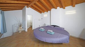 Ein Schlafzimmer mit einem großen Bett, Holzbalkendecke, weißen Wänden und Fliesenboden.