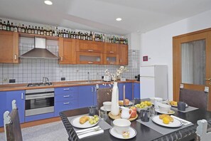 A modern kitchen with wooden cabinets, a gas stove, and a dining area with a table set for breakfast. - Samuel House- Lake view traditional Italy (Toscolano Maderno)