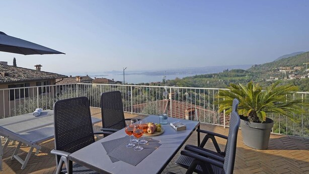 Eine Terrasse mit gedecktem Tisch für zwei Personen, mit Blick auf eine malerische Küstenstadt und Hügellandschaft.