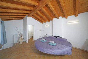 A bedroom with a large bed, wooden ceiling beams, white walls, and a tiled floor. - Samuel House- Two flats together (Toscolano Maderno)