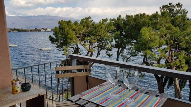 A balcony with a view of the sea, a wooden table, and two chairs. - Modern Flat with lake view & private beach! (Toscolano-Maderno)