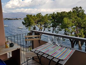 Un balcón con vista al mar, una mesa de madera y dos sillas.