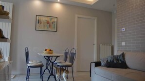 A living room with a sofa, a dining table with chairs, a cat, and a radiator. - Modern Flat with lake view & private beach! (Toscolano-Maderno)