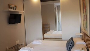 A hotel room with a large bed, a flat-screen TV mounted on the wall, a wooden nightstand, and a mirror reflecting the room. - Modern Flat with lake view & private beach! (Toscolano-Maderno)