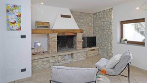 Ein gemütlicher Wohnbereich mit Kamin aus Stein, Fernseher und einer bequemen Sitzecke.