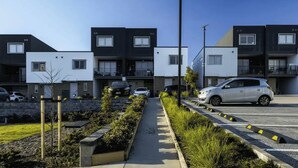 A modern residential building with a central walkway, parking spaces, and a street view.